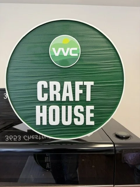 Project 106: VVC Craft House — round green property identification sign with routed woodgrain texture.