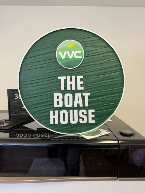 Project 107: VVC Boat House — round green property identification sign with routed woodgrain texture.