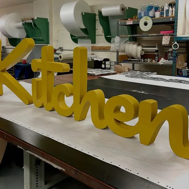Gold dimensional letters arranged on a sign-shop workbench
