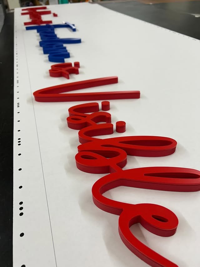 Red script acrylic letters laid out for a custom wall sign