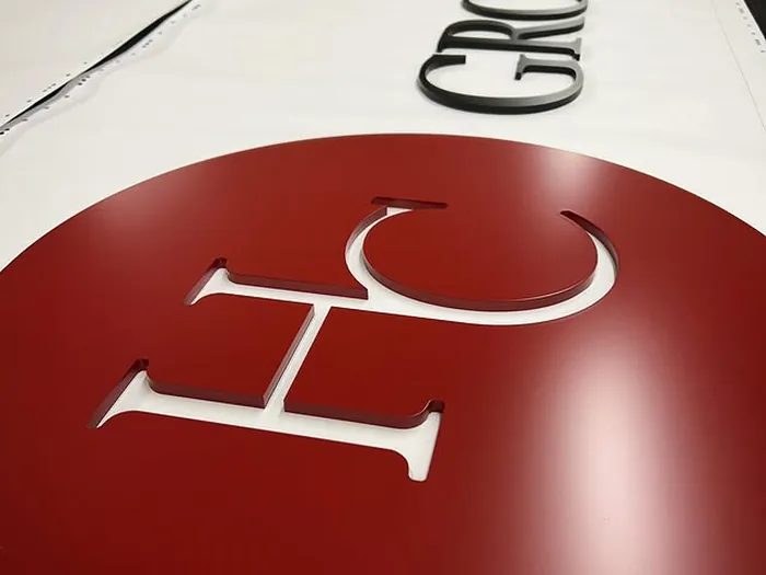 Red round logo panel with raised white acrylic initials